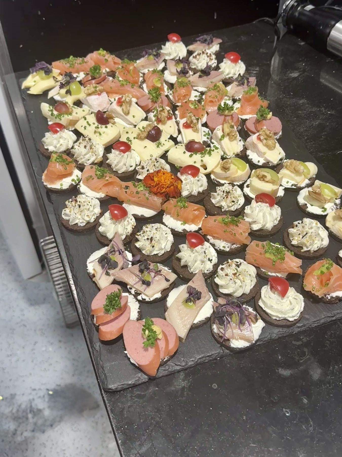 Feine Canapés mit Lachs, Brie und Trauben auf einer Schieferplatte